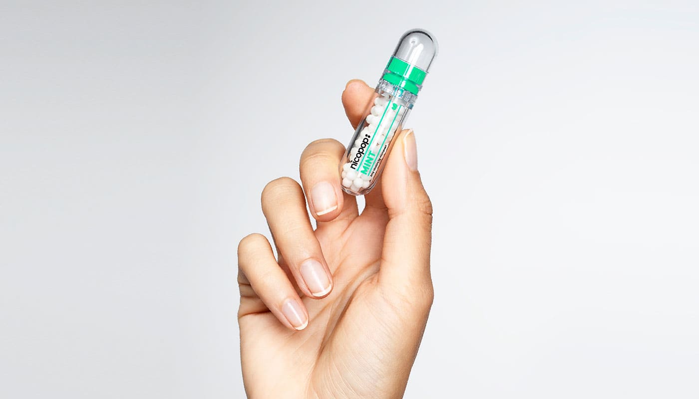 Woman holding a container of mint flavoured Nicopop nicotine pearls in her hand against a white and grey gradient background.